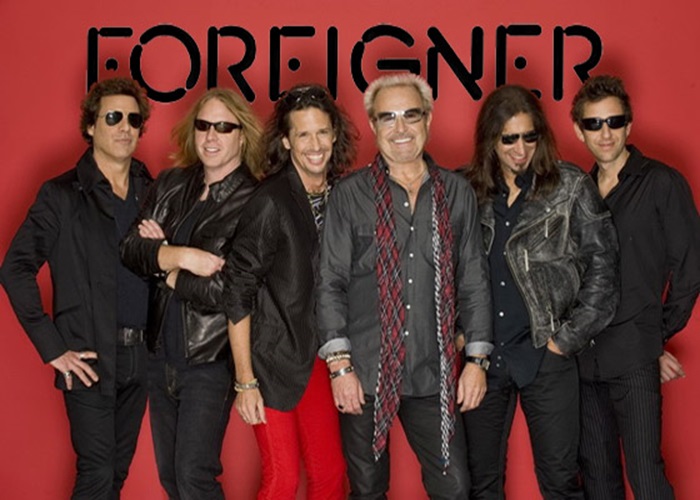 Снимка на Foreigner по време на концерт, изпълняващи своите известни рок хитове.