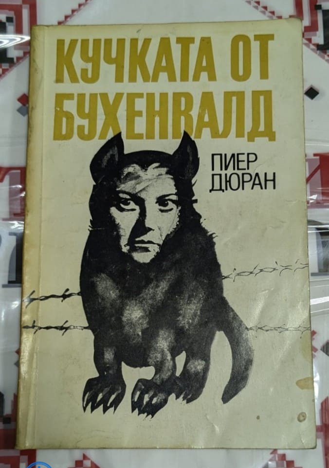 Корицата на книгата "Кучката от Бухенвалд" от Пиер Дюран (1985 г.), с изображение на куче с човешко лице, символизиращо жестокостта на нацистката надзирателка.