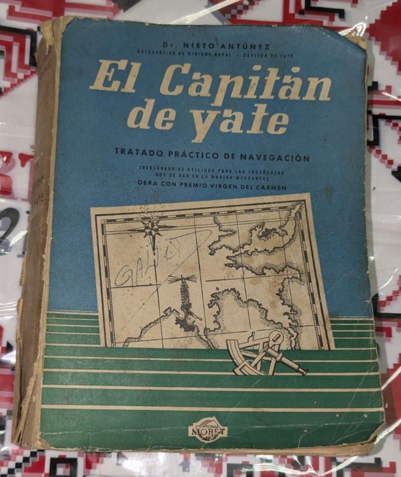 Стара книга със синьо-зелена корица, озаглавена „El Capitán de Yate“, с илюстрация на морска карта, компас и секстант.