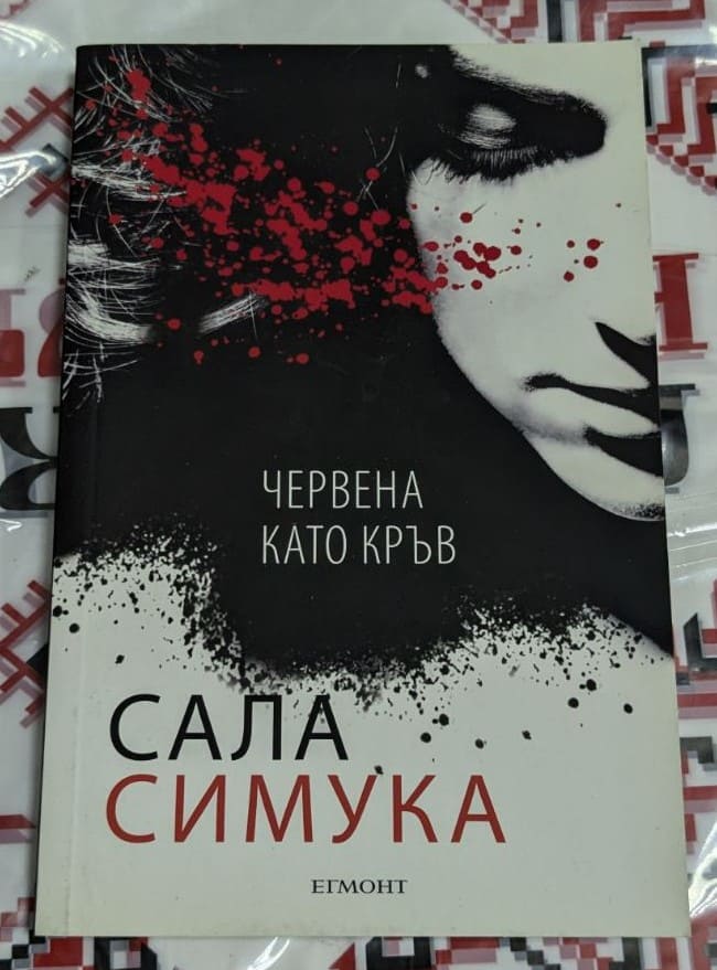 Корица на книгата Червена като кръв с интензивен червен фон и заглавие в контрастен бял шрифт, символизиращо кръвта и напрежението.