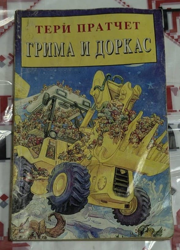 Корица на книгата „Грима и Доркас“ от Тери Пратчет, с илюстрация на жълт булдозер, пълен с гноми в движение, на син фон.