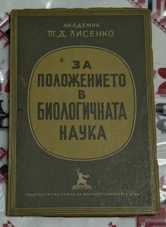 Открита антикварна книга „За положението в биологичната наука“ от Т. Д. Лисенко (1949), поставена върху традиционна покривка с народни мотиви.