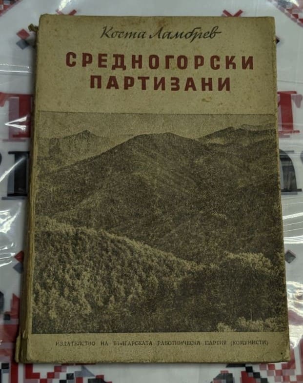 Корица и вътрешна страница на книгата „Средногорски партизани“ от Коста Ламбрев, издание на БКП, поставена върху народна шевица.