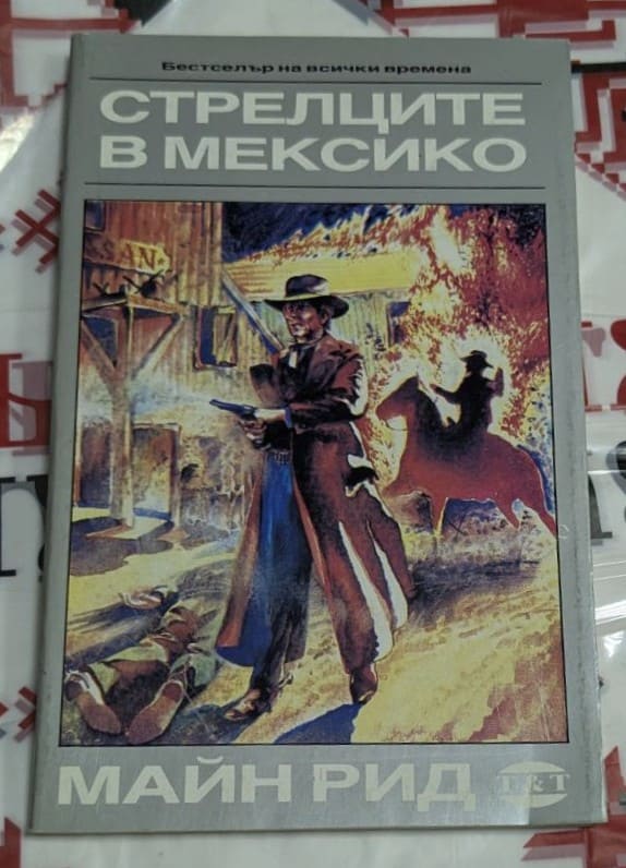 Корица на книгата „Стрелците в Мексико“ от Майн Рид с илюстрация на каубой пред горяща сграда и ездач на заден план, издадена на български език.